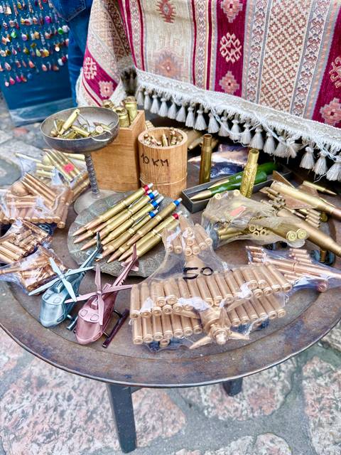       Market stall displaying polished brass bullet casings and crafted souvenirs arranged in plastic bags and trays.
  