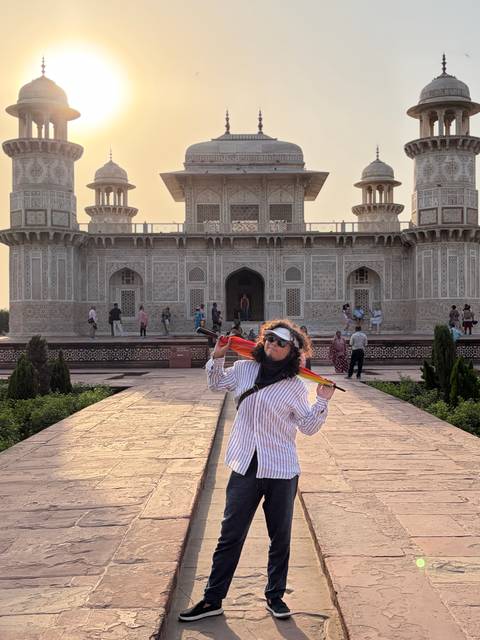       Traveller posing with a colourful umbrella in front of an ornate Mughal-style marble mausoleum courtyard.
  
