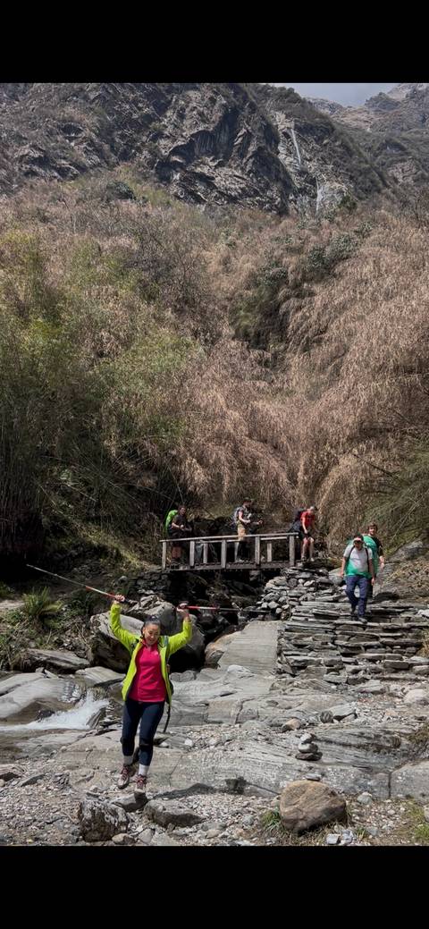       Small group of trekkers crossing a wooden bridge over a rocky stream in a dense valley forest.
  
