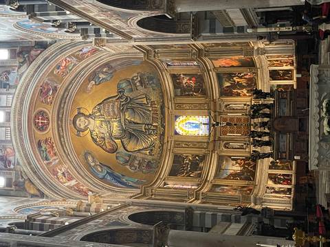       Lavishly decorated church apse with golden mosaic of Christ and ornate Renaissance paintings.
  