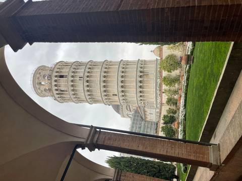       Iconic Leaning Tower of Pisa framed by an arched cloister opening with manicured garden below.
  