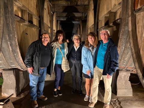       Group of travellers smiling inside a dimly lit historic wine barrel cellar.
  