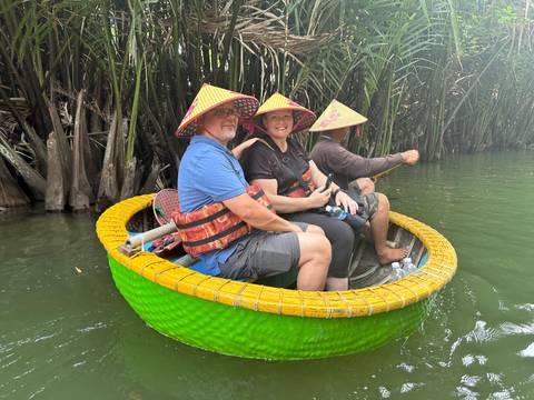      Travellers wearing conical hats ride in a vibrant green woven basket boat through mangrove palms.
  