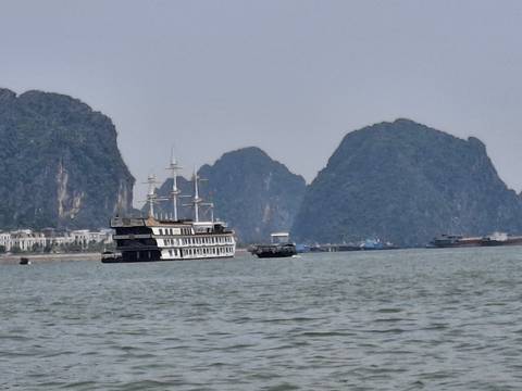       Cruise ship and small boats sail among towering limestone karst islands in a hazy bay.
  