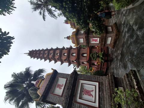       Tall red-brick multi-tiered pagoda surrounded by small shrines and greenery on an overcast day.
  