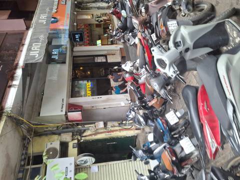       Street view with numerous parked motorbikes outside a small café in a busy urban Vietnamese lane.
  