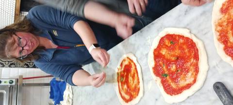       Participants adding basil to tomato-sauced pizza bases during a hands-on cooking class.
  