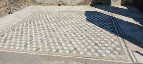       Stone mosaic floor in a 3-D cube pattern at an outdoor archaeological site.
  