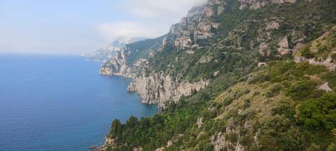       Sheer green-clad cliffs of the Amalfi Coast plunging into deep blue Mediterranean waters.
  