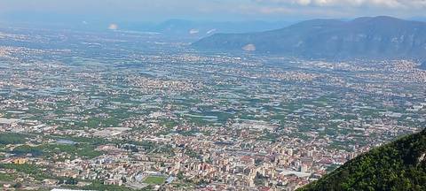       Zoomed aerial view of an Italian town and patchwork farmland with mountains beyond.
  