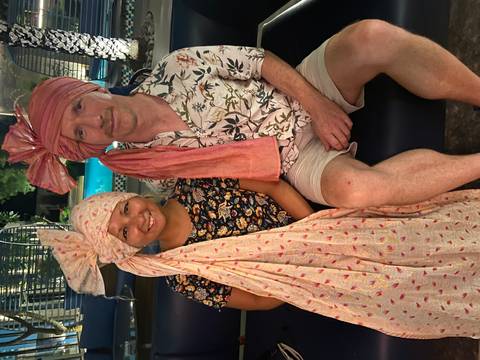       Man and woman wearing decorative turbans sit on a bench beside a softly lit pool at night.
  