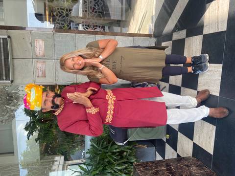       Visitor poses with a traditionally dressed mustachioed doorman, both greeting with folded hands outside a hotel entrance.
  
