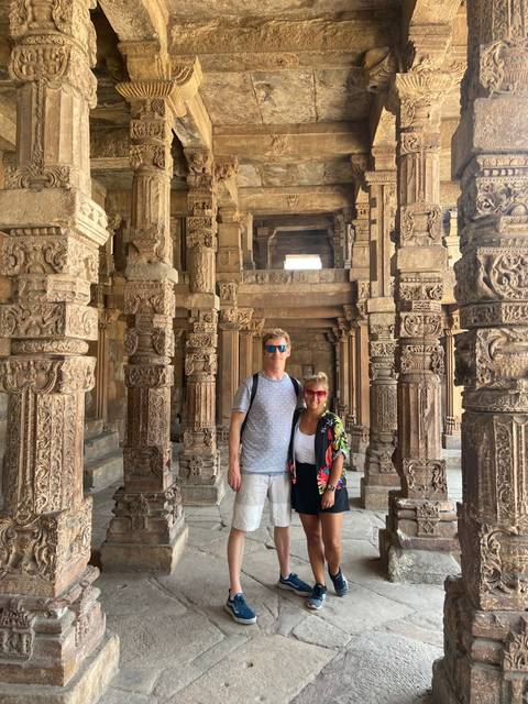       Couple standing among intricately carved stone pillars of an ancient Indian temple or stepwell.
  