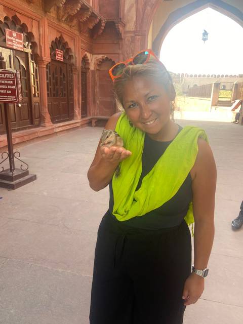       Smiling traveler holding a small squirrel in her hand within a sandstone courtyard.
  