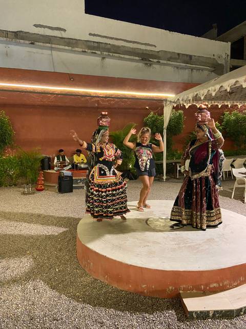       Traveler dances with two costumed Rajasthani folk dancers balancing pots during an outdoor evening show.
  