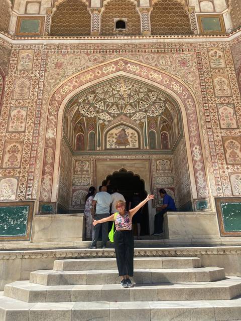       Traveler spreads arms joyfully in front of the ornate painted Ganesh Pol gate at Amber Fort.
  