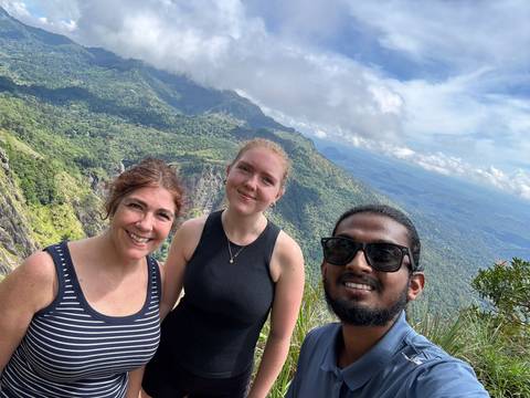      Selfie of three hikers on a mountain ridge with sweeping forested valleys stretching behind.
  