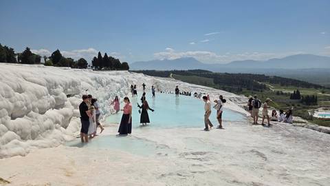       Crowds walk and wade in the turquoise thermal pools of Pamukkale's white travertine terraces.
  
