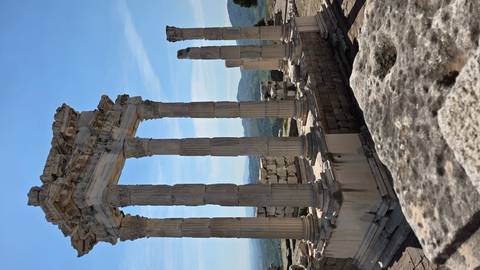       Impressive marble columns of an ancient hill-top temple ruin overlooking green valleys and distant mountains under a clear blue sky.
  