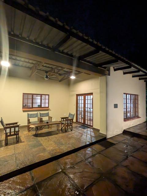       Simple covered patio with wooden chairs, a fan and tiled floor lit by warm ceiling lights.
  