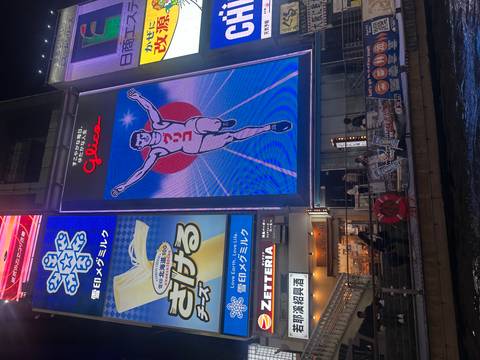       Iconic illuminated Glico running man sign towers above Dotonbori canal at night.
  