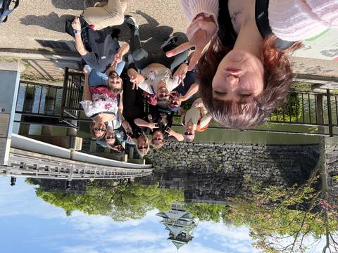       Tour group poses playfully by moat and stone walls with a castle in background.
  