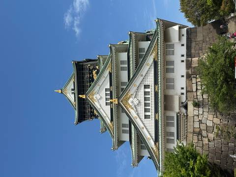       Grand white and green-tiled Osaka Castle rises against clear blue sky.
  