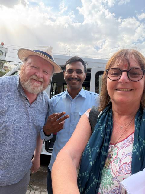      Smiling travellers taking a selfie with their driver beside a white van
  