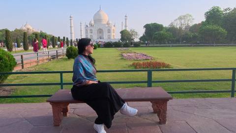       Woman seated on a bench with the Taj Mahal framed in the background.
  