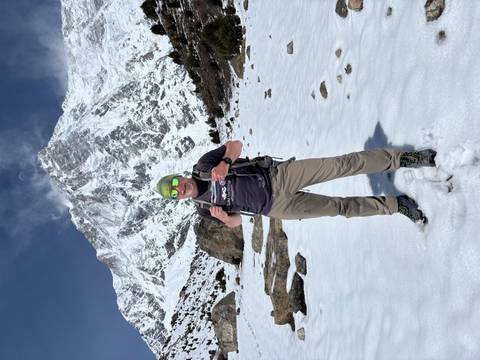       Smiling hiker posing on a snowy slope with towering Nanga Parbat in the background.
  