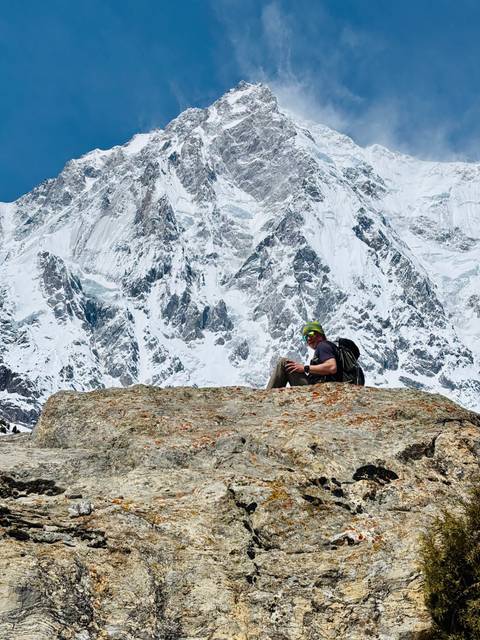       Traveler resting on a rocky ledge facing a sheer wall of ice-clad peaks.
  