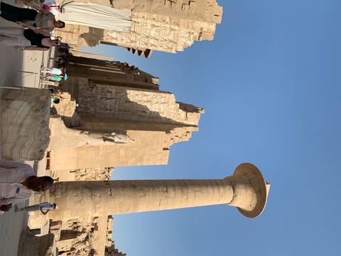       Massive column and ruined walls of Karnak Temple complex under clear blue sky.
  