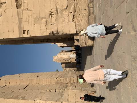       Visitors walk between tall sandstone pylons in an Egyptian temple courtyard.
  