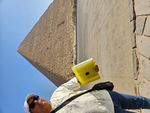       Person holding a yellow case standing near the Great Pyramid under a clear blue sky
  