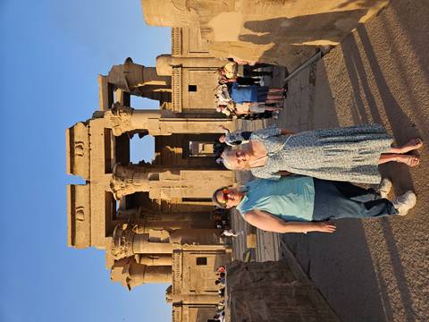       Two travellers posing in front of the stone columns of Kom Ombo Temple at golden hour
  
