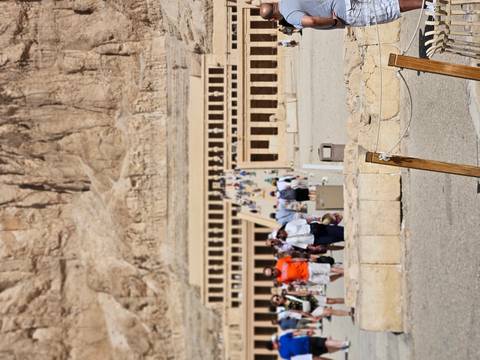       Visitors walking toward the terraced Temple of Hatshepsut backed by desert cliffs
  