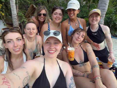       Beachgoers in swimwear take a cheerful close-up selfie with drinks and a beer bottle.
  