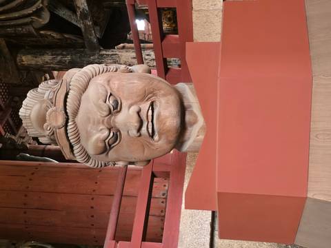      Close-up of a fierce wooden guardian head sculpture inside a Japanese temple.
  