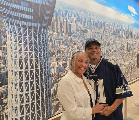      Smiling couple poses before a large photo backdrop of Tokyo Skytree and city skyline.
  