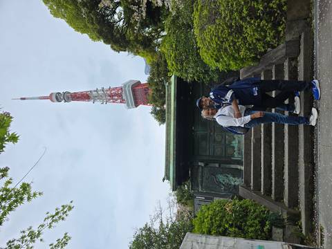       Couple embraces on stone steps with Tokyo Tower rising behind lush greenery.
  