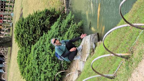       Traveler crouches by a koi pond in a manicured Japanese garden, reaching toward the water.
  
