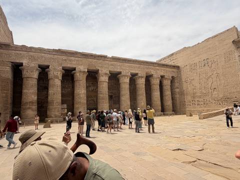       Visitors explore a vast Egyptian temple courtyard lined with carved stone columns.
  