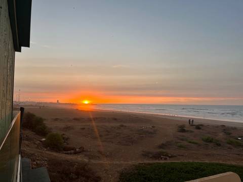       Brilliant orange sun sets over the Atlantic as gentle waves lap a wide Moroccan beach.
  