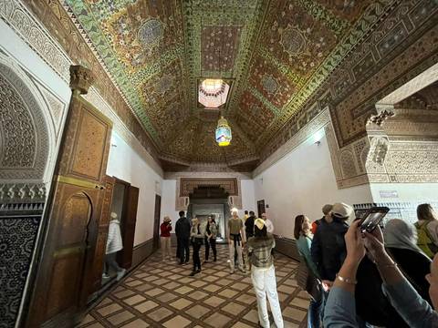       Tourists explore an ornately decorated hall with detailed mosaic ceilings in Morocco.
  