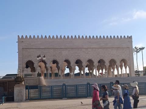       The Mausoleum of Mohammed V with its ornate arches and tourists passing in front.
  