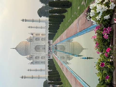       Iconic frontal view of the Taj Mahal with reflection in the long water channel and flowers in foreground.
  