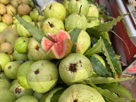       Close-up of fresh green guavas with a pink-fleshed fruit cut open.
  