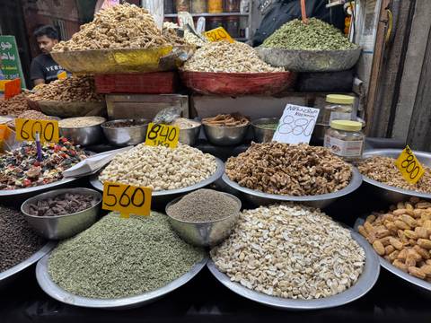       Assorted nuts, seeds and spices displayed in metal bowls with handwritten price tags at a market.
  