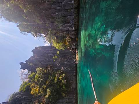       Sheer limestone walls rise above emerald lagoon waters dotted with kayakers under bright tropical sunlight.
  