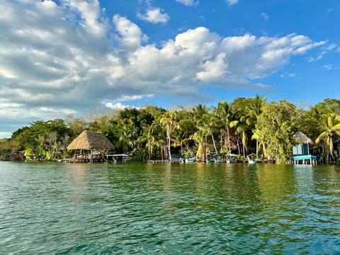       Tropical riverside lined with thatched huts and lush palms under a partly cloudy sky in Río Dulce.
  